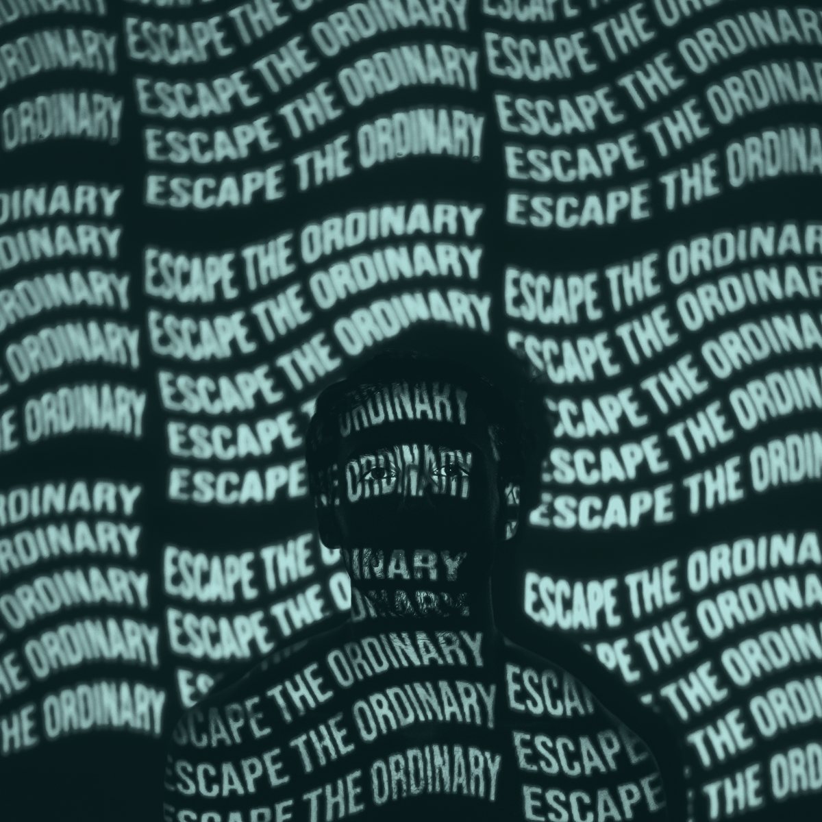 A person lit by a projection of the repeated phrase “Escape the ordinary”, the words falling across their face and body