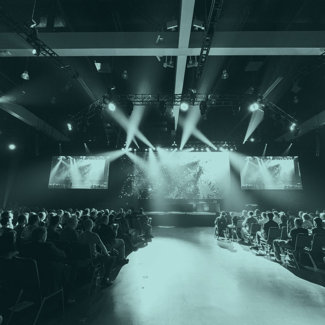 A production desk at a live event, stage lights and an audience out of focus beyond it
