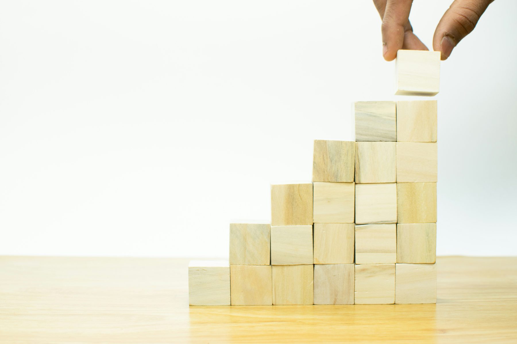 A hand placing the last wooden block on a staircase of blocks that grows higher with each step